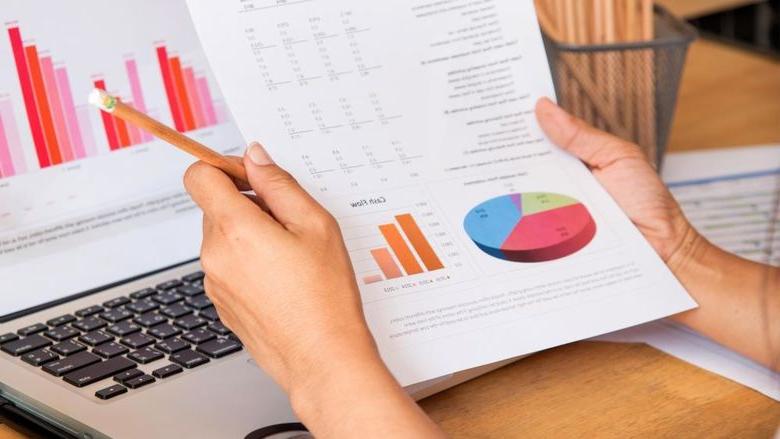 A woman reviews information on an Excel spreadsheet, with graphs, both on paper and on a computer screen.